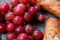 A bunch of juicy large red grapes and fresh crispy wheaten baguette on a table of dark old wooden boards Royalty Free Stock Photo
