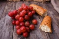 A bunch of juicy large red grapes and fresh crispy wheaten baguette on a table of dark old wooden boards Royalty Free Stock Photo