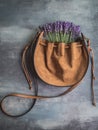 Bunch of lavenders in crossbody leather orange bag. Concrete background.