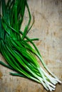 Bunch of long stem green fresh scallions on weathered wood background, top view, minimalist