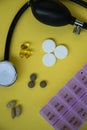 Bunch of pills and capsules, box for storage of drugs and medical stethoscope and blood pressure meter on yellow background, healt