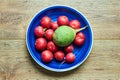Bunch of pink radishes and one big green lies on a blue plate on a wooden tabletop