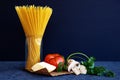 Bunch of raw spaghetti in a glass jar. Dry pasta with cheese, tomato and mushroom on dark blue background Royalty Free Stock Photo