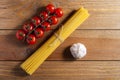 Bunch of raw spaghetti tied with rope, tomatoes cherry and bulb of garlic on brown wooden background