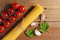 Bunch of raw spaghetti tied with rope, tomatoes cherry, slices of garlic, parsley leaves and pepper on brown wooden background.