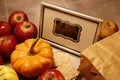 A bunch of red apples lies next to a miniature pumpking. A framed blank chalkboard sign stands in the middle