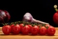 Bunch of red cherry tomatoes wet in water drops on wooden board. Garlic, onion and red sweet pepper in drops of moisture Royalty Free Stock Photo