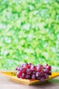Bunch of red grapes on yellow orange plate, against green blur background Royalty Free Stock Photo