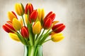 Bunch of red and yellow tulip flowers in a glass vase against colored plaster Royalty Free Stock Photo