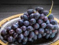 Bunch of ripe blue-black table grape with leaf served on black plate on black wooden background Royalty Free Stock Photo