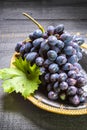 Bunch of ripe blue-black table grape with leaf served on black plate on black wooden background Royalty Free Stock Photo