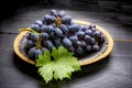 Bunch of ripe blue-black table grape with leaf served on black plate on black wooden background Royalty Free Stock Photo