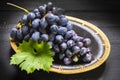 Bunch of ripe blue-black table grape with leaf served on black plate on black wooden background Royalty Free Stock Photo