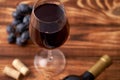 A bunch of ripe blue grapes with a glass of red wine with wine corks nearby, and a sealed bottle of red wine on a textured wooden Royalty Free Stock Photo