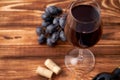 A bunch of ripe blue grapes with a glass of red wine with wine corks nearby, and a sealed bottle of red wine on a textured wooden Royalty Free Stock Photo