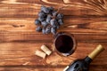 A bunch of ripe blue grapes with a glass of red wine with wine corks nearby, and a sealed bottle of red wine on a textured wooden Royalty Free Stock Photo