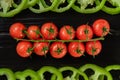 Bunch of ripe red cherry tomatoes and ring chopped green sweet pepper on black wooden board. Top view branch of tomatoes Royalty Free Stock Photo