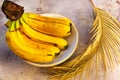 Bunch of ripe yellow bananas on brown concrete background. Still life with fresh organic fruits on the plate and palm tree leaf. Royalty Free Stock Photo