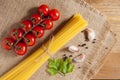 Bunch of spaghetti. To her left are cherry tomatoes. Slices of garlic, pepper and petrunka leaves are on the right. All this on a