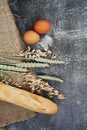 Bunch of spikelets of wheat, baguette and bakery ingredients on dark wooden background. Copy space
