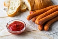 Bunch of thin smoked sausages, ketchup and slices of bread on a white wooden table. Sausage and fresh vegetables as a source of Royalty Free Stock Photo