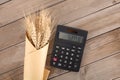 A bunch of wheat ears wrapped in kraft paper and a calculator on the table Royalty Free Stock Photo