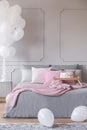 Bunch of balloons in elegant grey bedroom interior with king size bed with grey bedding and pink pillows and blanket Royalty Free Stock Photo