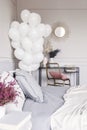 Bunch of white balloons in trendy bedroom interior with industrial dresser with golden mirror and bed with grey sheets