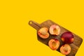 Bunch of whole cut in half juicy raw fresh nectarines on wooden board on yellow background. Summer fruits healthy plant based diet