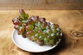 A bunch of wild grapes in a white ceramic plate on a wooden background