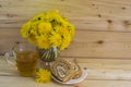 A bunch of yellow dandelions. A glass of tea in a glass mug. Two slices of honey roll with cream. Royalty Free Stock Photo