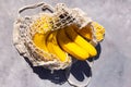 Bunch of yellow ripe bananas in avoska on grey background with sharp shadows. String bag with fresh organic fruits on the floor.