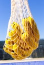 Bunch of yellow ripe bananas in avoska. String bag with fresh organic fruits against blue sky background. Selective focus. Blurred