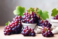 Bunches of dark grapes with green leaves in a white plate on the table. Ripe black red grapes. Fresh harvest Royalty Free Stock Photo