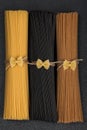 Bunches of different types of Italian spaghetti. Black, brown and yellow spaghetti on gray background