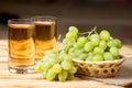 Bunches of fresh ripe green grapes in wicker basket on piece of sackcloth and two glasses with grape juice on a wooden textured ba Royalty Free Stock Photo