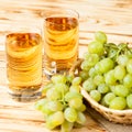 Bunches of fresh ripe green grapes in wicker basket on piece of sackcloth and two glasses with grape juice on a wooden textured ba Royalty Free Stock Photo