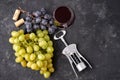Bunches of ripe green and blue grapes with a glass of red wine, a corkscrew and wine corks on a dark stone background. Top view. Royalty Free Stock Photo