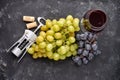 Bunches of ripe green and blue grapes with a glass of red wine, a corkscrew and wine corks on a dark stone background. Top view. Royalty Free Stock Photo