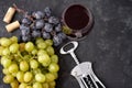 Bunches of ripe green and blue grapes with a glass of red wine, a corkscrew and wine corks on a dark stone background. Top view. Royalty Free Stock Photo