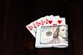 A bundle of dollars tied with an elastic band and a combination of playing cards on a dark wooden table. Lucky win