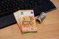 A bundle of Euro banknotes on a computer keyboard. Near a roll of one hundred dollars Royalty Free Stock Photo