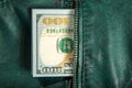 A bundle of hundred-dollar bills sticks out of the pocket of a leather jacket of green color