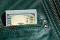 A bundle of hundred-dollar bills sticks out of the pocket of a leather jacket of green color