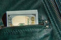 A bundle of hundred-dollar bills sticks out of the pocket of a leather jacket of green color. Shooting close-up