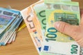 a bundle of money, 50 and 100 euros clutched in hand, a pile of smaller denomination banknotes lying on the table next to it,