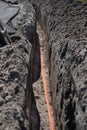 Bundle of orange fiber optic cables lie in a dug trench in the ground in a street