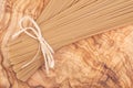 Bundle of Organic uncooked Brown Rice Spaghetti pasta tied with straw on a natural olive wood cutting board .