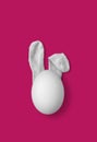 Bunny rabbit ears made of white fluffy socks with white egg on bright pink background. Easter minimal concept. Flat lay