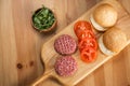 Buns, raw beef cutlets, tomatoes and herbs for burgers cooking